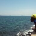 ragazza africana che si affaccia da una terrazza sugli scogli e guarda verso il mare dell'Isola di Gorée