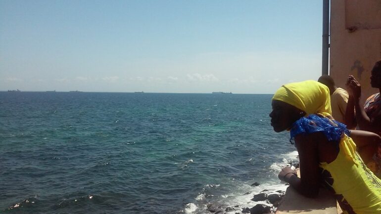 ragazza africana che si affaccia da una terrazza sugli scogli e guarda verso il mare dell'Isola di Gorée